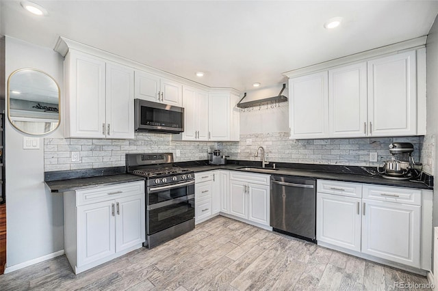 kitchen featuring a sink, tasteful backsplash, dark countertops, appliances with stainless steel finishes, and white cabinets