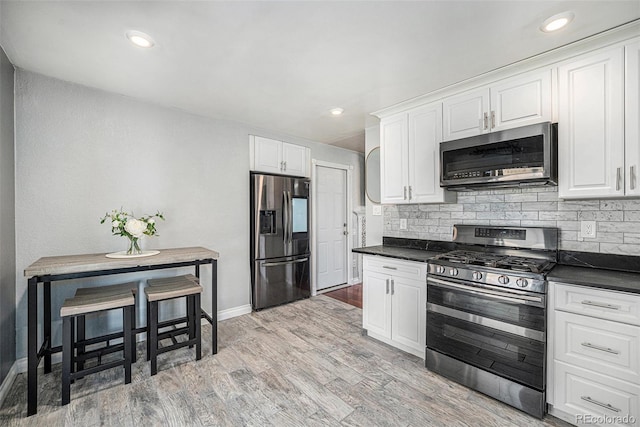 kitchen with dark countertops, backsplash, appliances with stainless steel finishes, and white cabinets