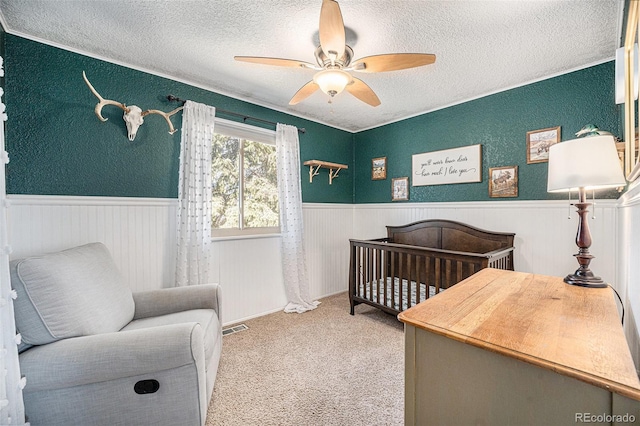 carpeted bedroom featuring a textured ceiling, ceiling fan, and wainscoting