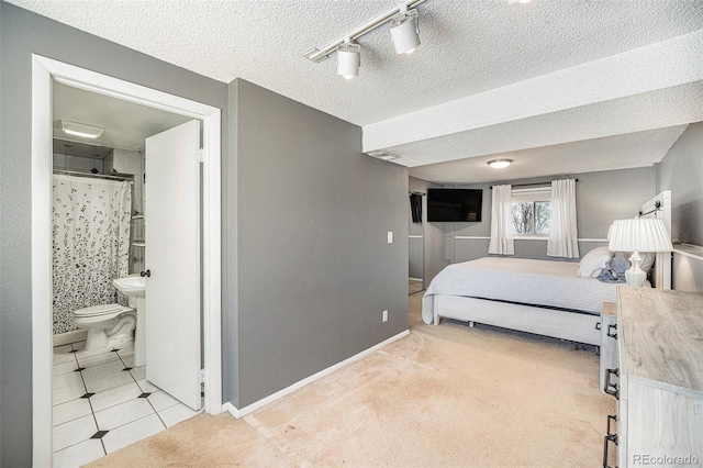 bedroom with light carpet, a textured ceiling, ensuite bath, light tile patterned floors, and baseboards