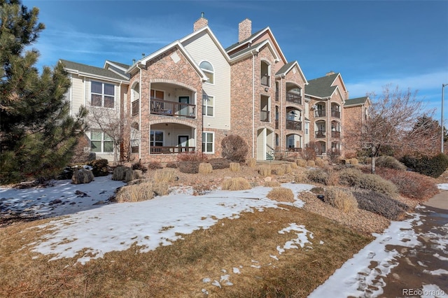 view of front of property featuring stone siding, a chimney, and a balcony