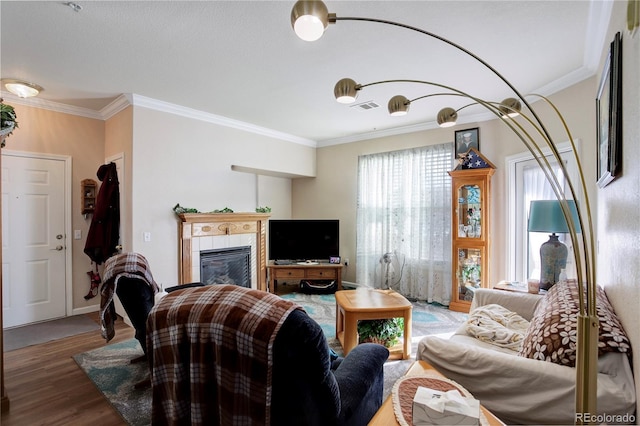 living room featuring ornamental molding, a tiled fireplace, wood finished floors, and visible vents