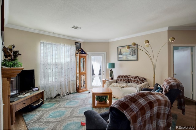 living room featuring a textured ceiling, visible vents, wood finished floors, and ornamental molding