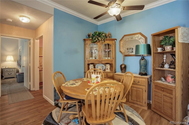 dining room with light wood finished floors, ceiling fan, baseboards, and crown molding