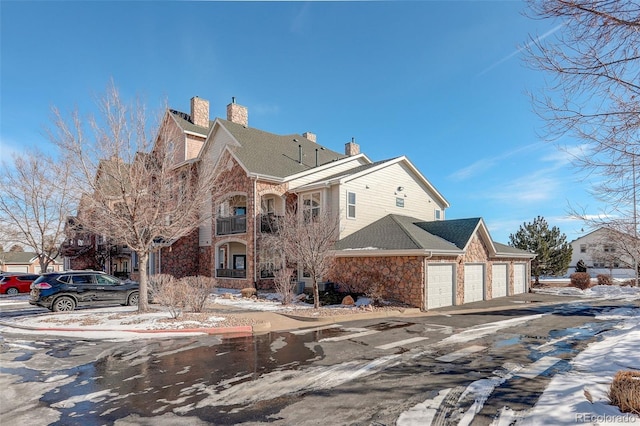 19049 E Warren Dr Unit 105, Aurora, CO 80013 - view of snow covered exterior featuring stone siding, a chimney, a garage, a shingled roof, and driveway