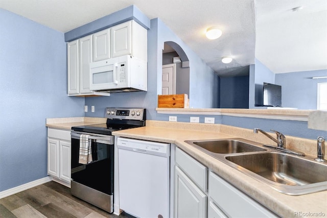 kitchen with white appliances, a sink, dark wood-type flooring, baseboards, and white cabinets