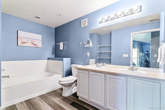 bathroom featuring a textured wall, wood finished floors, a garden tub, toilet, and double vanity