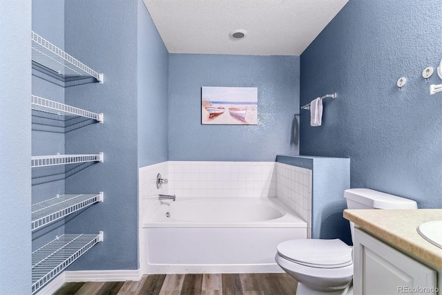 bathroom featuring wood finished floors, a bath, a textured wall, toilet, and vanity