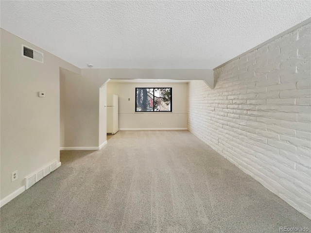 carpeted empty room featuring brick wall and a textured ceiling