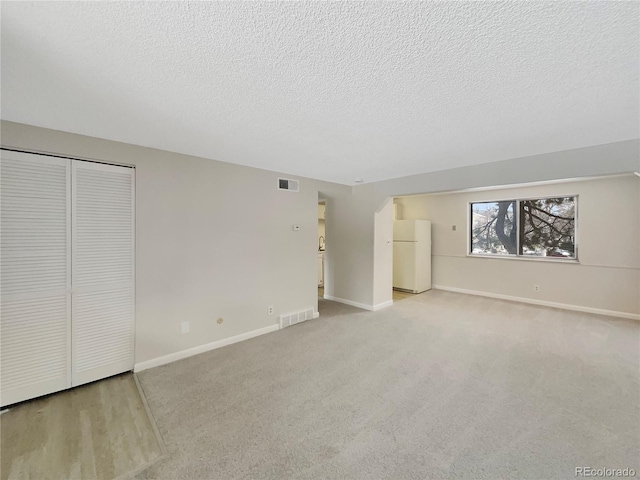 unfurnished bedroom with light colored carpet, a closet, white refrigerator, and a textured ceiling