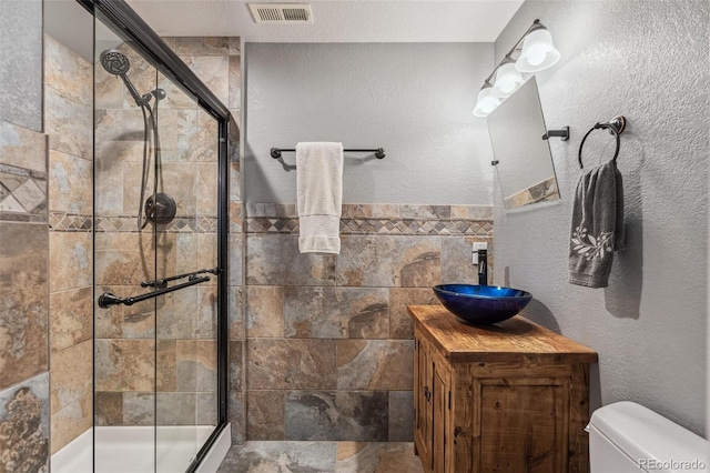 full bath featuring a textured wall, toilet, vanity, visible vents, and tiled shower