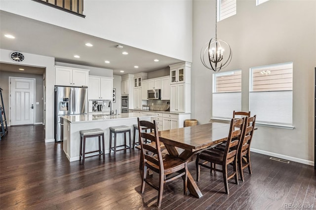 dining space with dark wood-style flooring, a notable chandelier, visible vents, a high ceiling, and baseboards