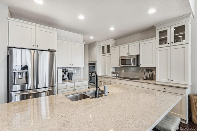 kitchen with tasteful backsplash, glass insert cabinets, stainless steel appliances, and a sink