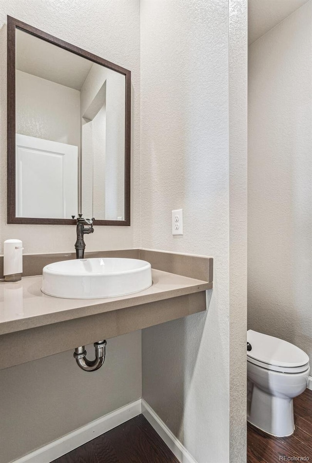 half bathroom featuring baseboards, a sink, toilet, and wood finished floors