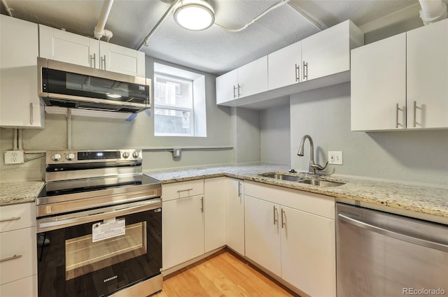 kitchen with light stone countertops, a sink, stainless steel appliances, white cabinets, and light wood-type flooring