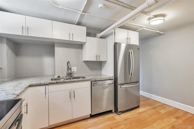 kitchen with a sink, light stone counters, light wood finished floors, white cabinets, and appliances with stainless steel finishes
