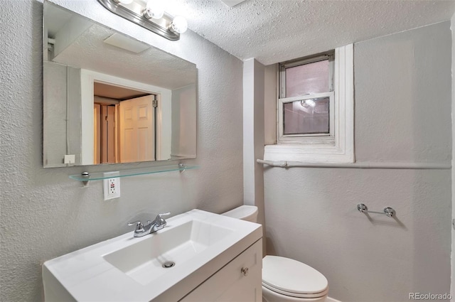 half bathroom featuring vanity, toilet, a textured wall, and a textured ceiling