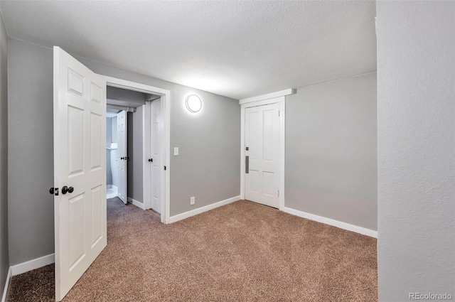 empty room featuring a textured ceiling, carpet, and baseboards