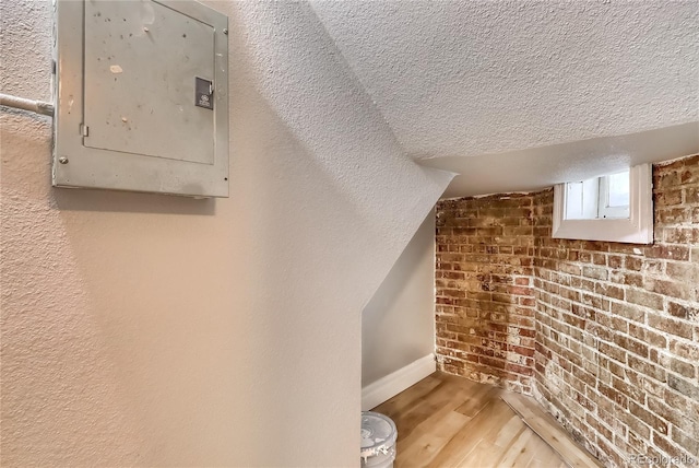additional living space featuring electric panel, a textured ceiling, baseboards, and wood finished floors