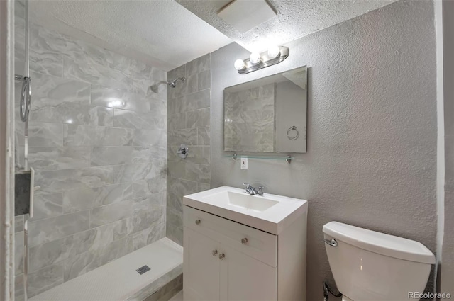 bathroom featuring a tile shower, vanity, toilet, and a textured wall