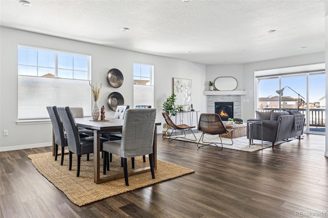 dining space with a stone fireplace, plenty of natural light, wood finished floors, and baseboards