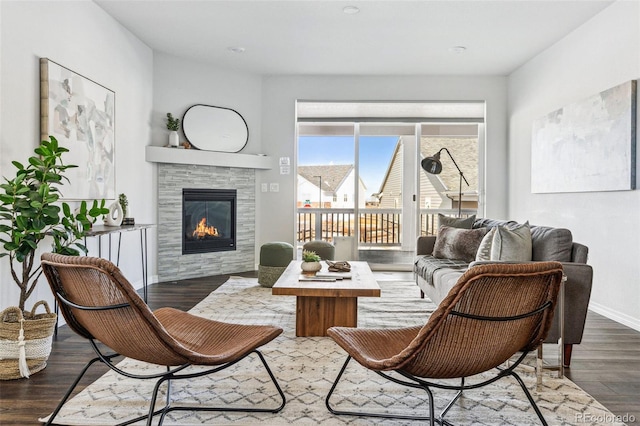 living area featuring a tiled fireplace, baseboards, and wood finished floors