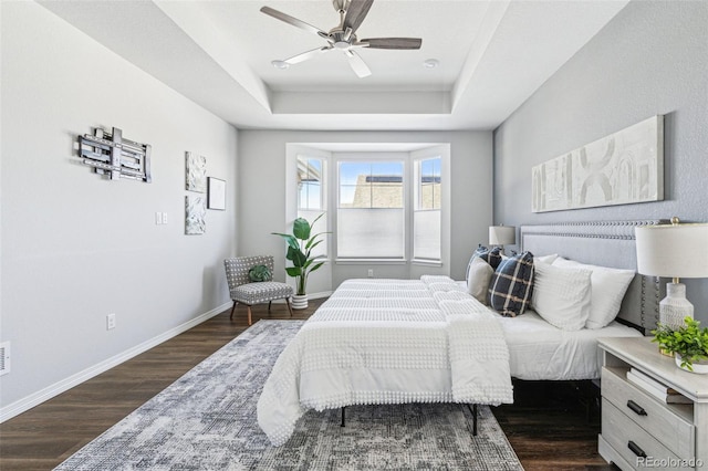 bedroom with a raised ceiling, wood finished floors, baseboards, and ceiling fan