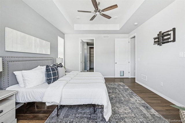 bedroom featuring visible vents, baseboards, a tray ceiling, and wood finished floors