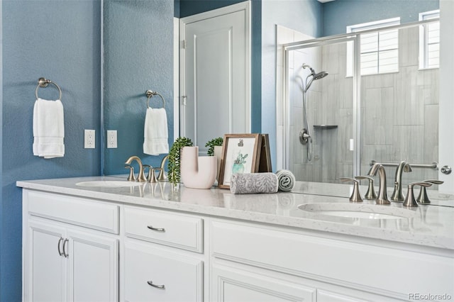 full bath with a sink, a stall shower, double vanity, and a textured wall