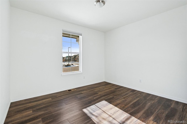 spare room with baseboards, visible vents, and dark wood-style flooring