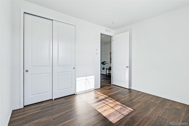 unfurnished bedroom with visible vents, baseboards, dark wood-type flooring, and a closet