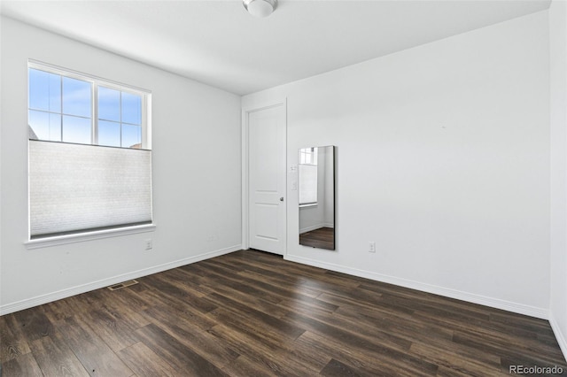 spare room with dark wood-style floors, visible vents, and baseboards