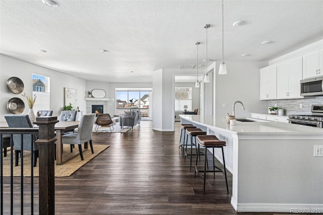 kitchen with stainless steel appliances, sink, an island with sink, hanging light fixtures, and a stone fireplace