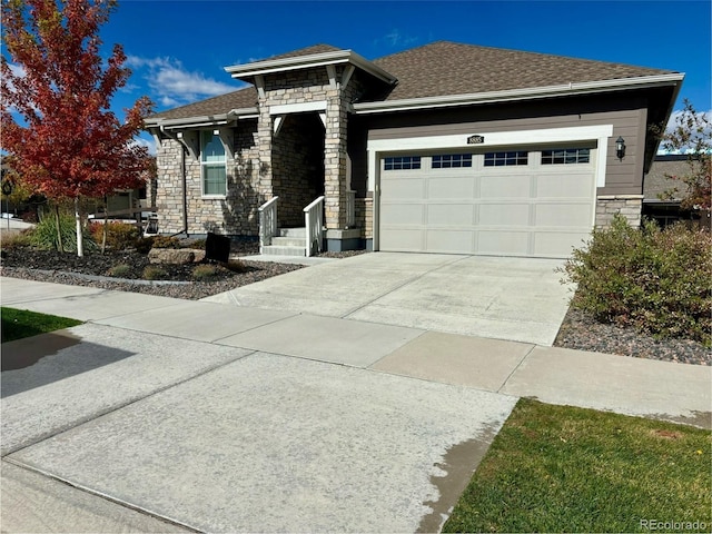 prairie-style home with stone siding, driveway, a shingled roof, and a garage