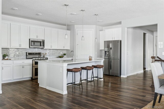 kitchen featuring a breakfast bar area, appliances with stainless steel finishes, a center island with sink, and white cabinetry