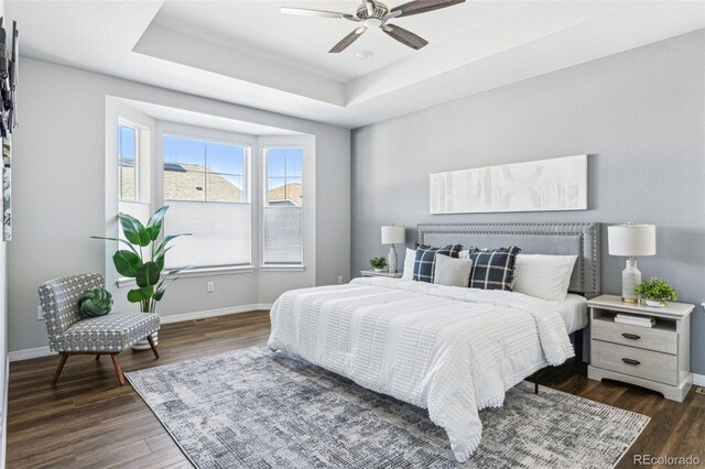 bedroom with a ceiling fan, a tray ceiling, wood finished floors, and baseboards