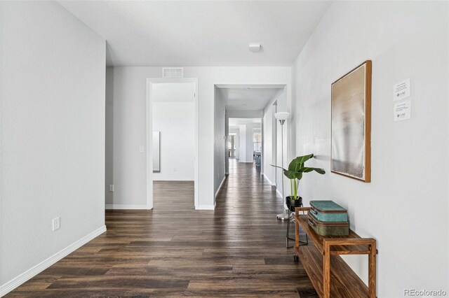 hall featuring visible vents, baseboards, and dark wood-style floors