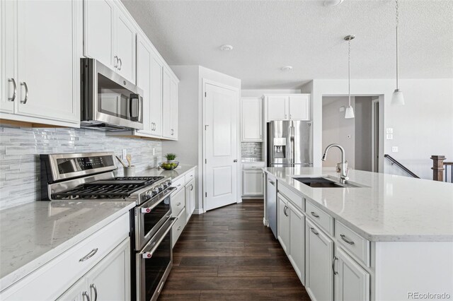 kitchen with a kitchen island with sink, a sink, dark wood finished floors, stainless steel appliances, and white cabinets