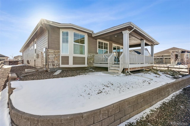 snow covered back of property featuring stone siding and covered porch