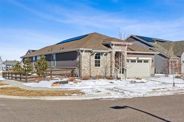 view of front facade with fence, roof with shingles, roof mounted solar panels, a garage, and stone siding