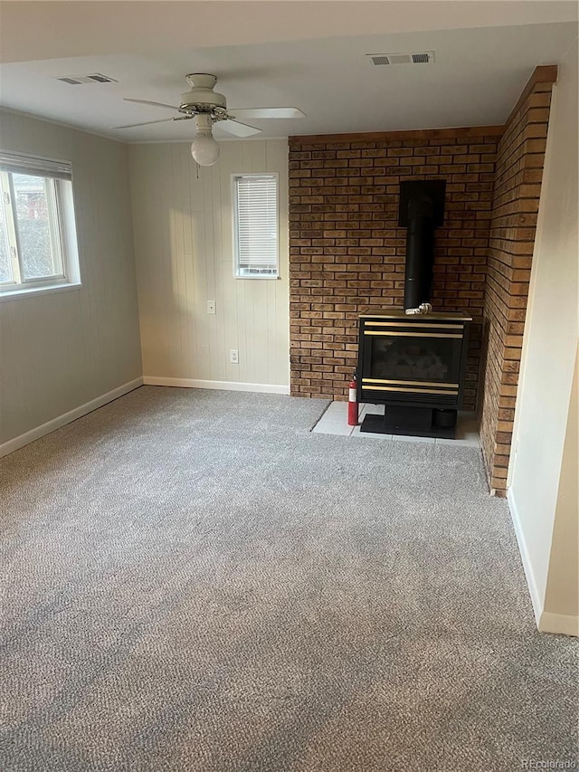 unfurnished living room with carpet flooring, brick wall, ceiling fan, and a wood stove