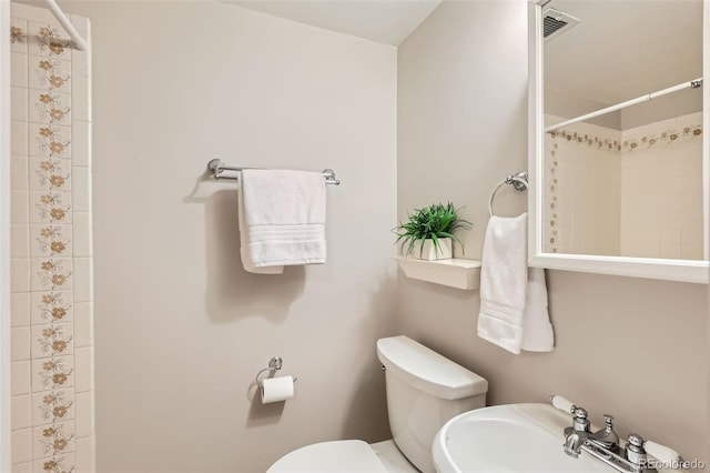 bathroom featuring toilet, tiled shower, and a sink