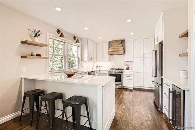 kitchen with open shelves, a peninsula, custom range hood, wine cooler, and high quality appliances