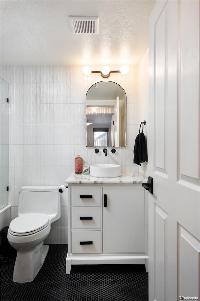 bathroom featuring tile walls, tile patterned flooring, vanity, toilet, and a textured ceiling