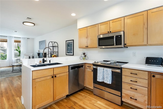 kitchen featuring appliances with stainless steel finishes, sink, light wood-type flooring, and kitchen peninsula