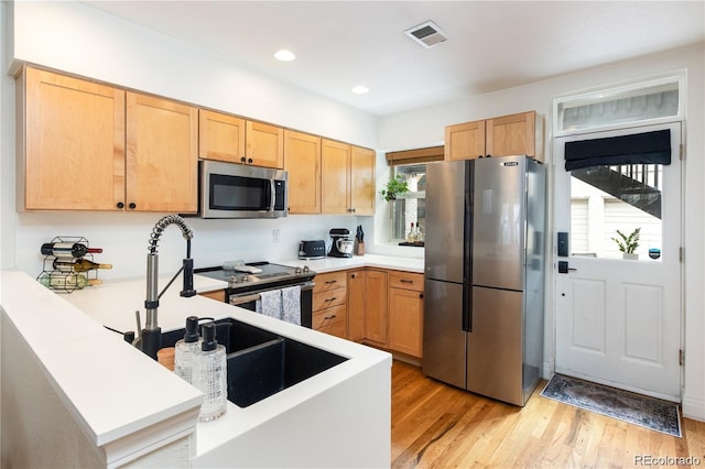 kitchen with stainless steel appliances, kitchen peninsula, light brown cabinets, and light wood-type flooring