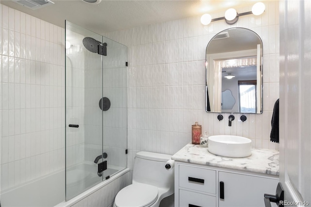 full bathroom featuring toilet, combined bath / shower with glass door, tile walls, vanity, and decorative backsplash