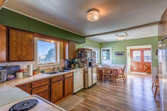 kitchen with light wood-type flooring, a textured ceiling, white appliances, and sink