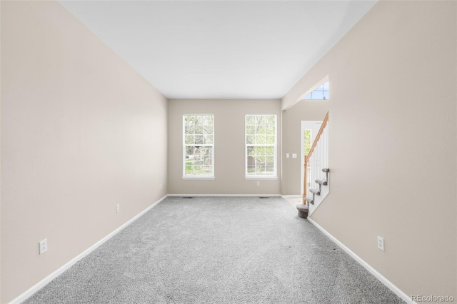 carpeted empty room with stairs and baseboards