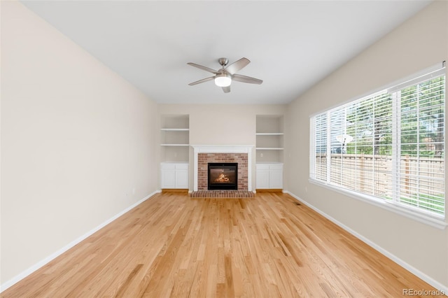unfurnished living room with baseboards, built in shelves, light wood-style flooring, and a ceiling fan